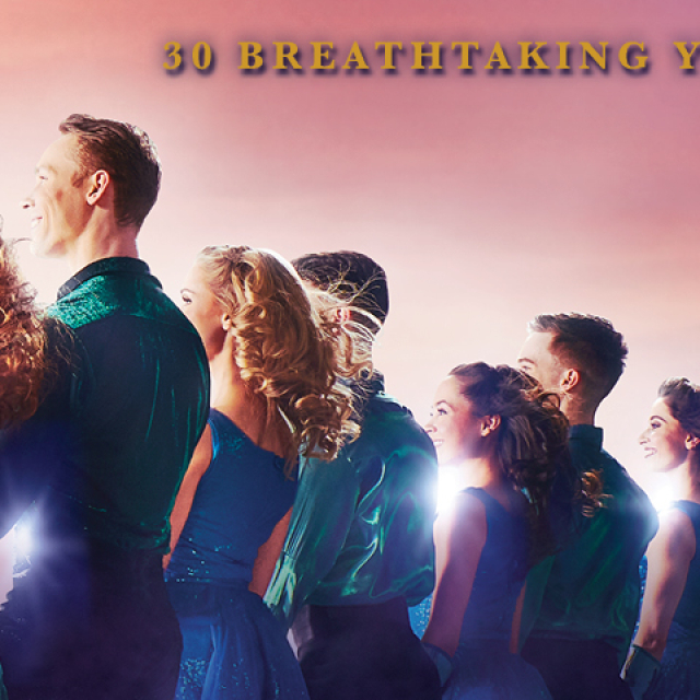 14 people wearing blue and green dance outfits facing away from the viewer, looking towards the sun