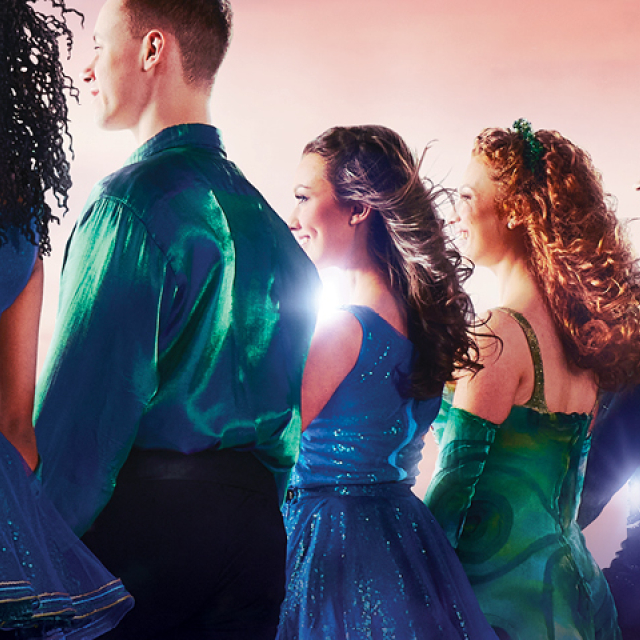 Promotional banner for Riverdance 30: The New Generation featuring a line of dancers in blue and green costumes illuminated by bright stage lighting against a pink and purple sky background. Gold text reads, “30 Breathtaking Years One Worldwide Phenomenon,” alongside the Riverdance 30: The New Generation logo. The dancers are shown in profile, standing shoulder to shoulder across the width of the image.